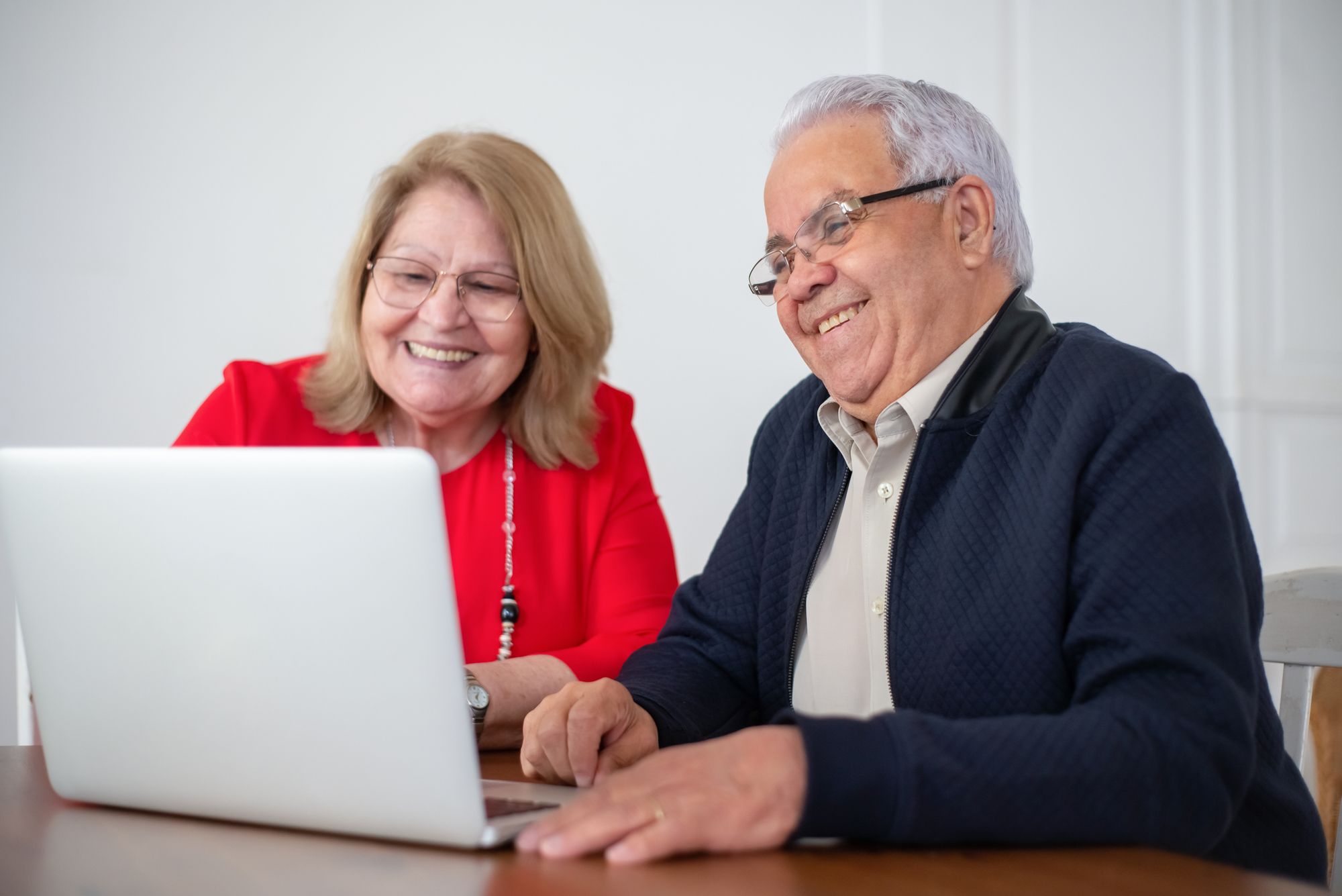 Casal maduro sorrindo enquanto usa um notebook em casa, imagem ilustrativa